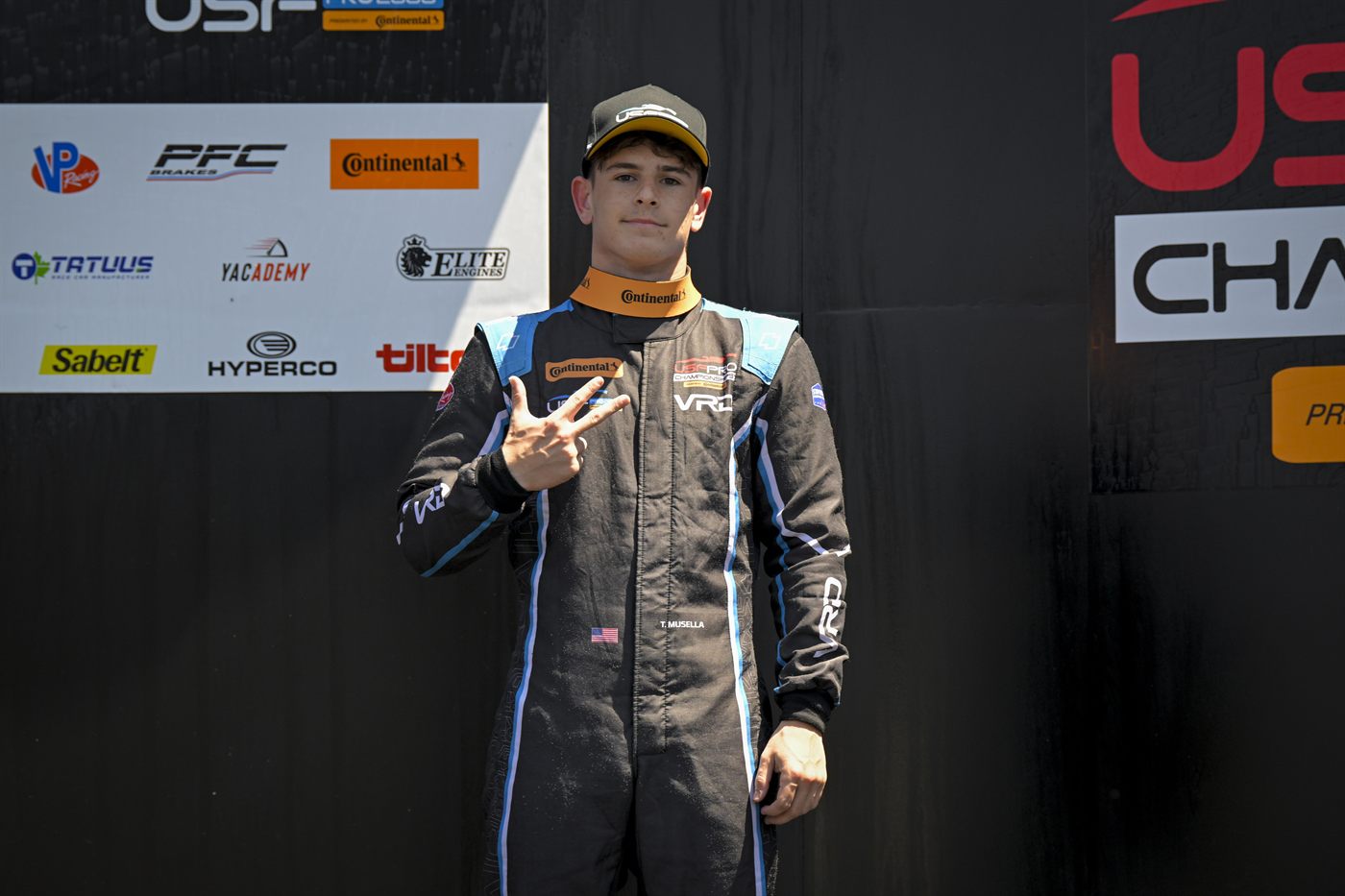 Musella on the podium steps at Indianapolis Motor Speedway holding up three fingers.